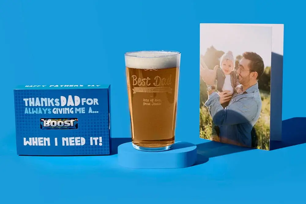Fathers Day gift set on a blue background featuring a personalised pint glass, a thank you gift box, and a photo card showing an adult holding a child outdoors